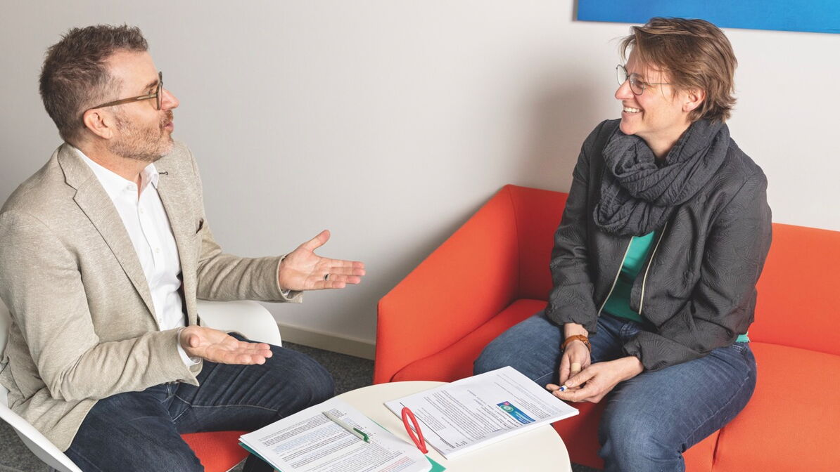 Cornelis Kooijman und Christina Zweifel sitzen sich in einem Büro gegenüber und sprechen miteinander.
